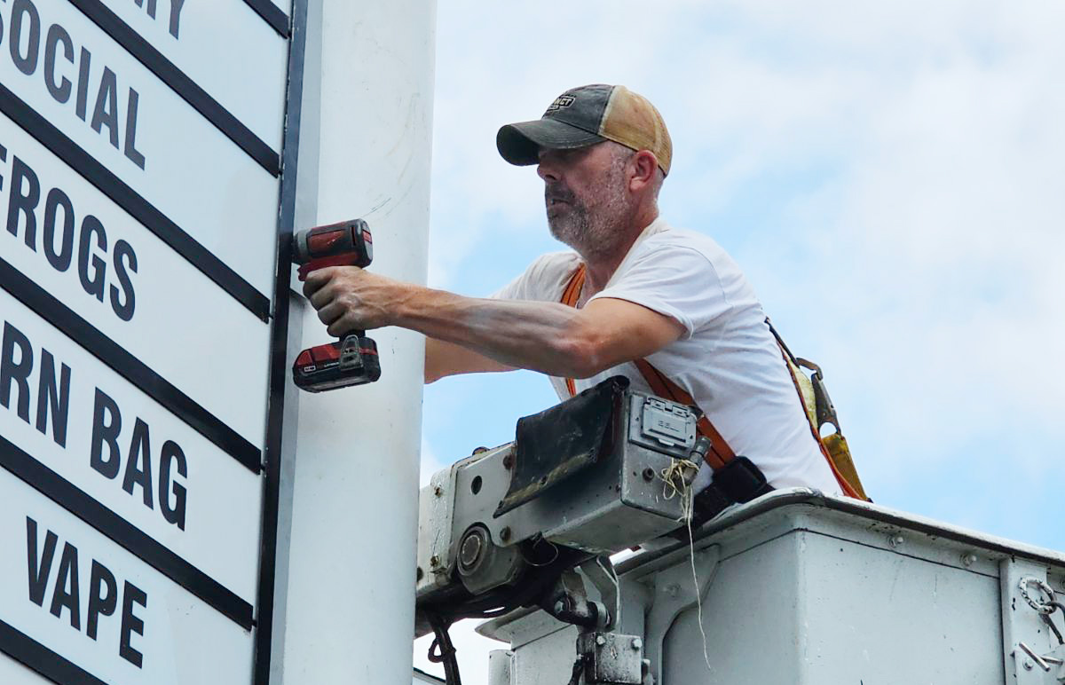 Technician installing new tenant name panels on a multi-tenant pylon sign at Eagle Village during a sign refresh.